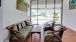 A room with two wooden sofas and a coffee table, a large window with a view of buildings and greenery, and a door leading outside. - Hotel O Panorama Rinjani LodgeNearTaman Nasional Gunung Rinjani (Sembalun Lawang)