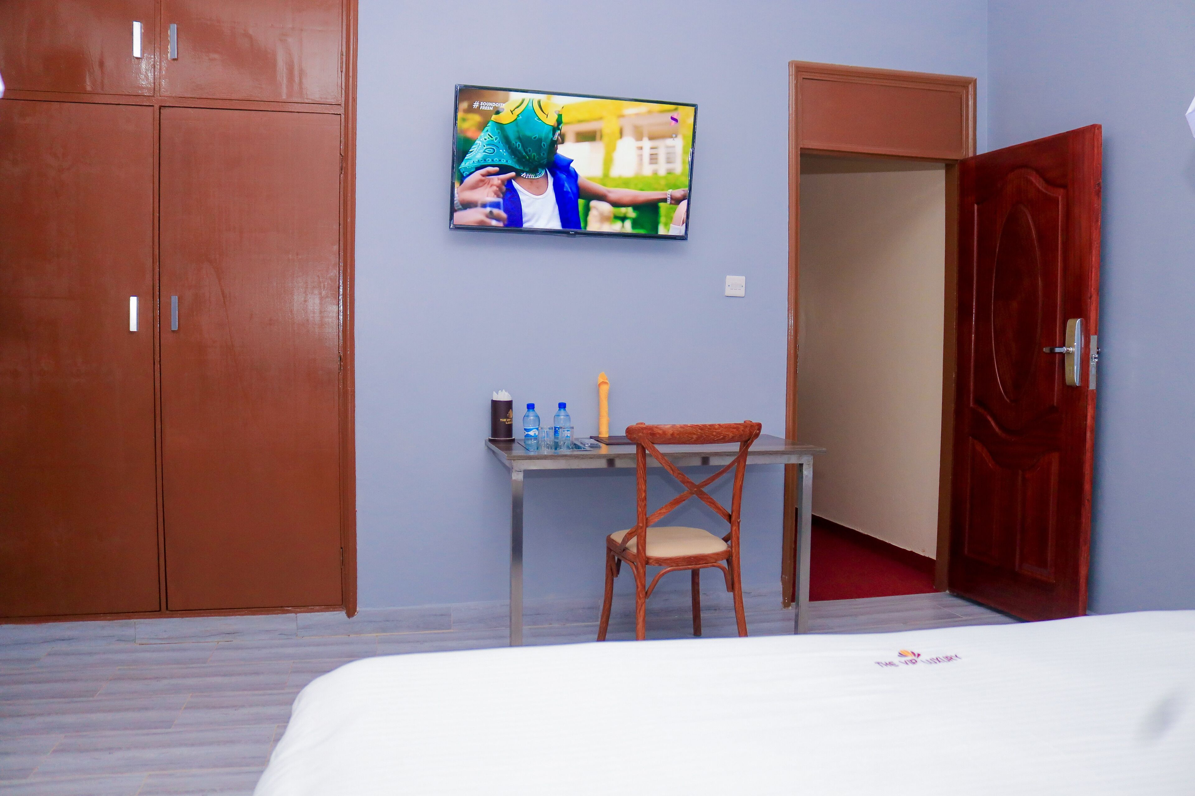 Una habitación de hotel con una cama, un escritorio con una silla, un televisor fijado a la pared y un armario.