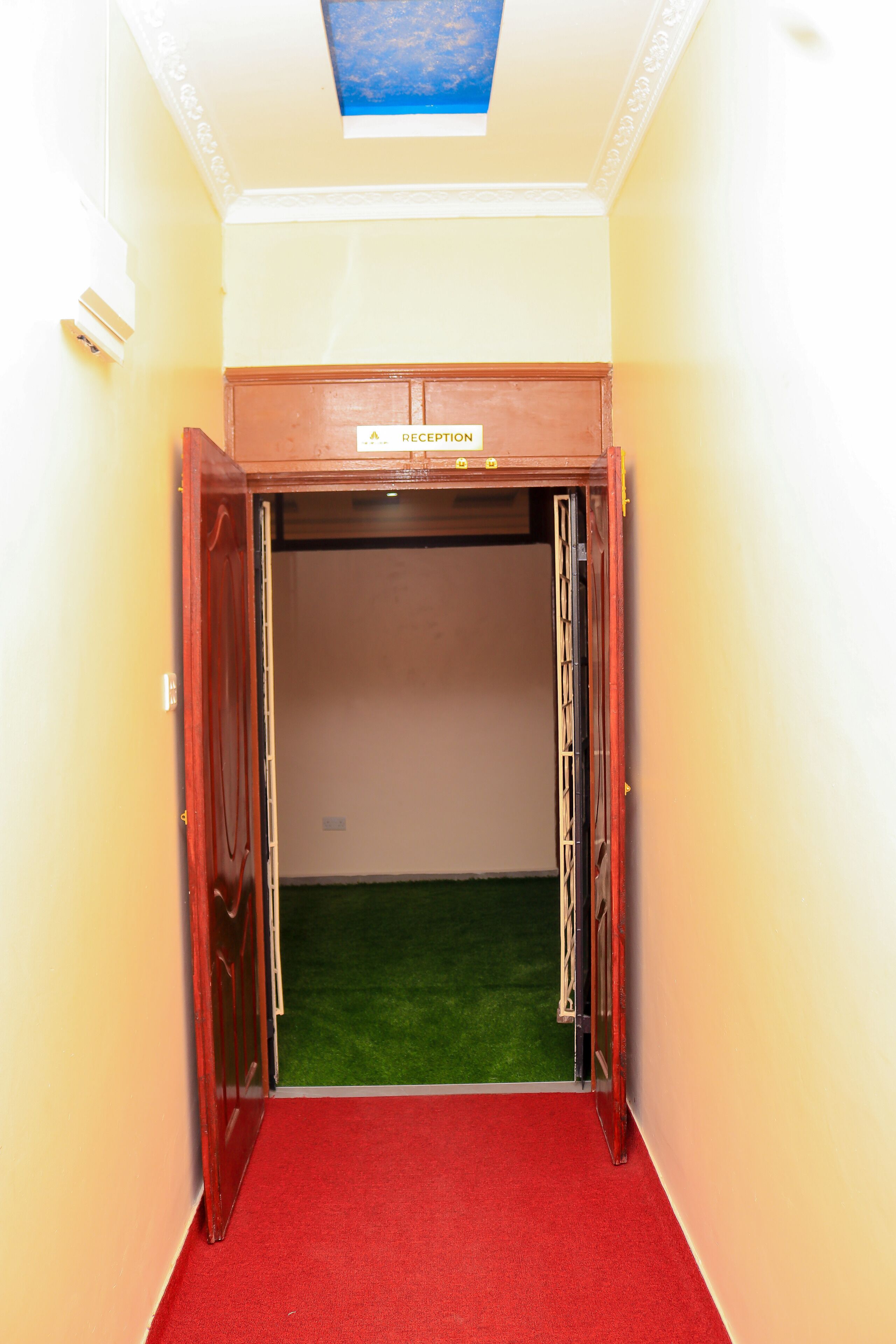 Un área de recepción con una alfombra roja que lleva a una puerta con la inscripción 'RECEPTION'.
