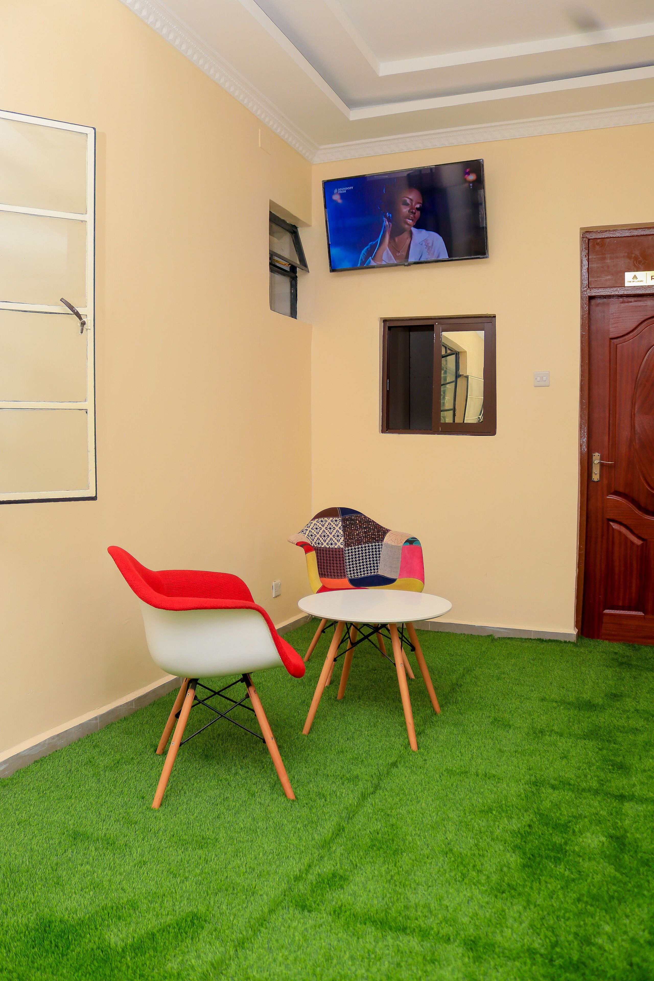 A room with a television mounted on the wall, a small table with a chair, and a door.