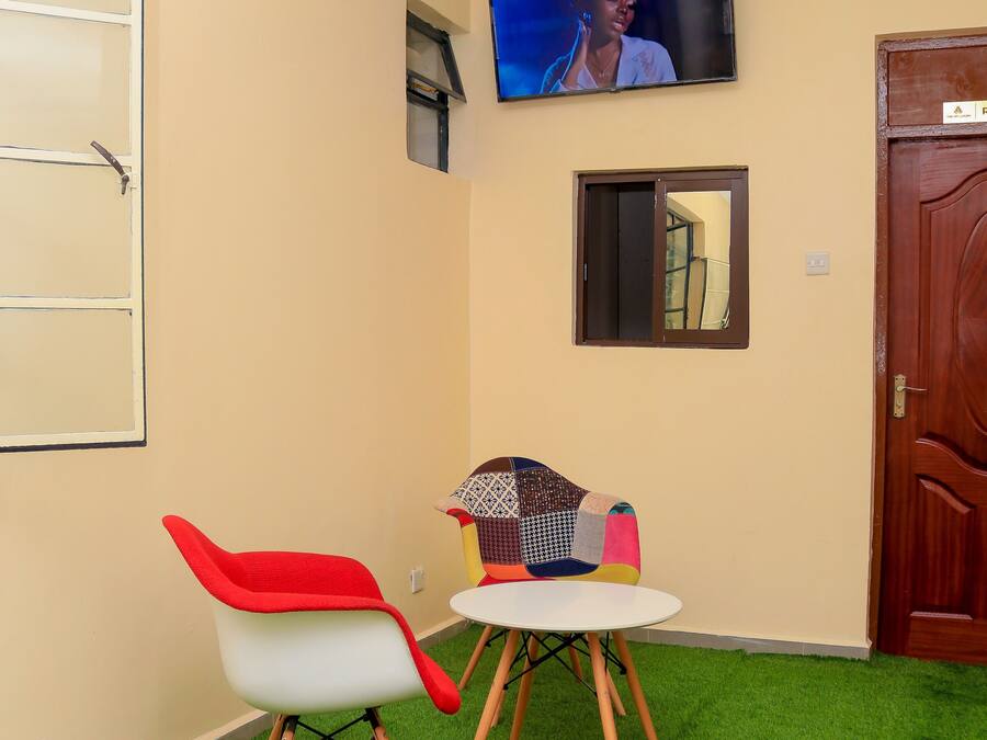 Una habitación con una televisión montada en la pared, una pequeña mesa con una silla y una puerta.