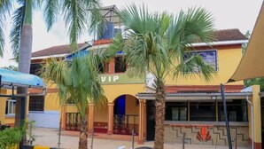 A building with a yellow facade, a blue entrance, and palm trees in front.
