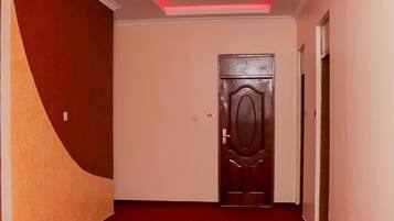 Un pasillo con alfombra roja, una puerta de madera y un techo blanco con iluminación empotrada.