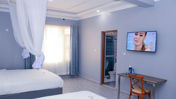 A hotel room with two beds, a desk, a TV, and a bathroom visible through an open door.