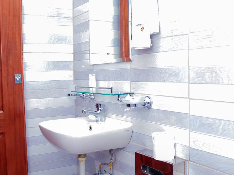 Un baño con un lavabo blanco, un estante de vidrio, una puerta de madera y un dispensador de papel higiénico.