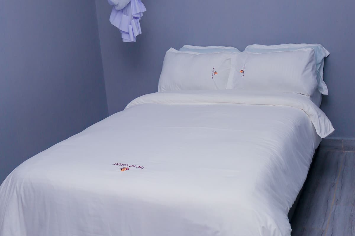 A neatly made bed with white linens in a room with light blue walls and a wooden floor.