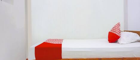 A single bed with a red and white bedspread, two pillows, one with a red pattern, and a wooden headboard.