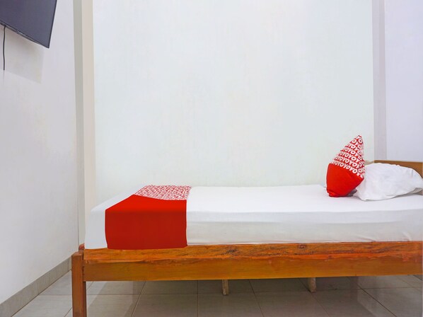 A single bed with a red and white bedspread, two pillows, one with a red pattern, and a wooden headboard.