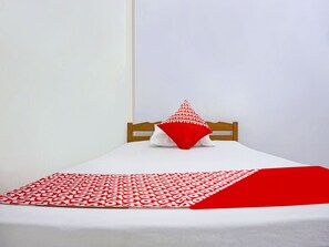 A bed with a white sheet, a red and white patterned blanket, and a red pillow. - Hotel O Kilana Homestay (Makassar)