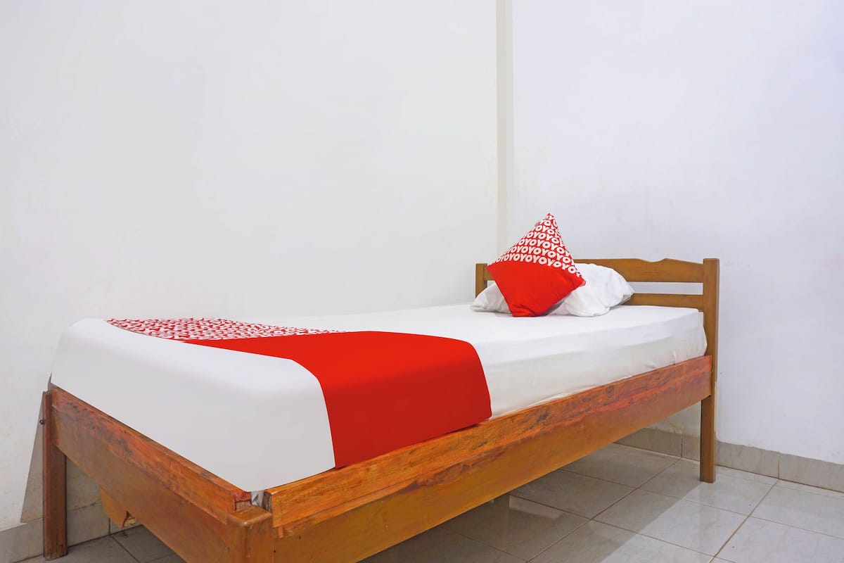 A single bed with a wooden frame, white bedding, and a red and white patterned pillow.