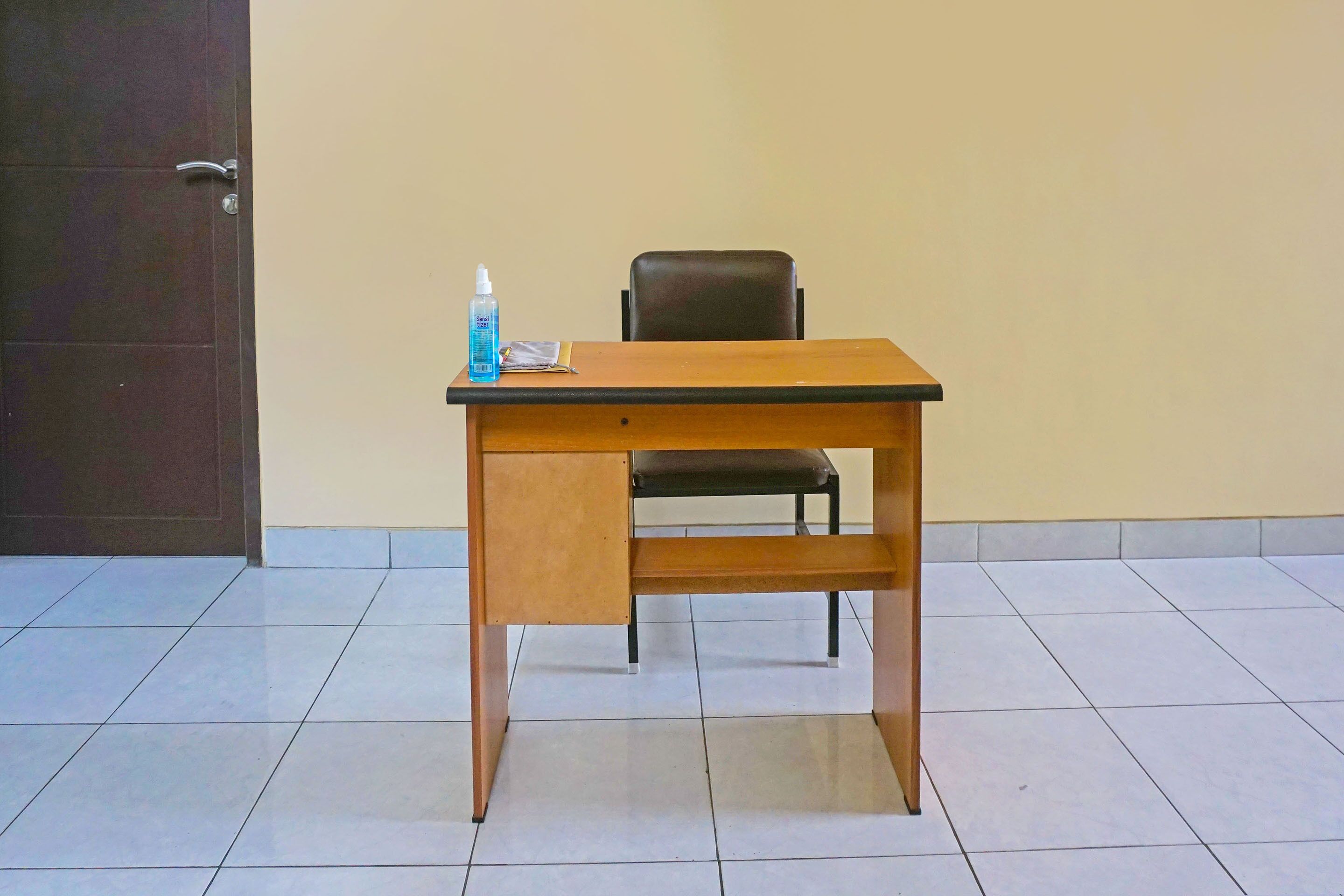 A wooden desk with a chair, a bottle of hand sanitizer, and a notepad.
