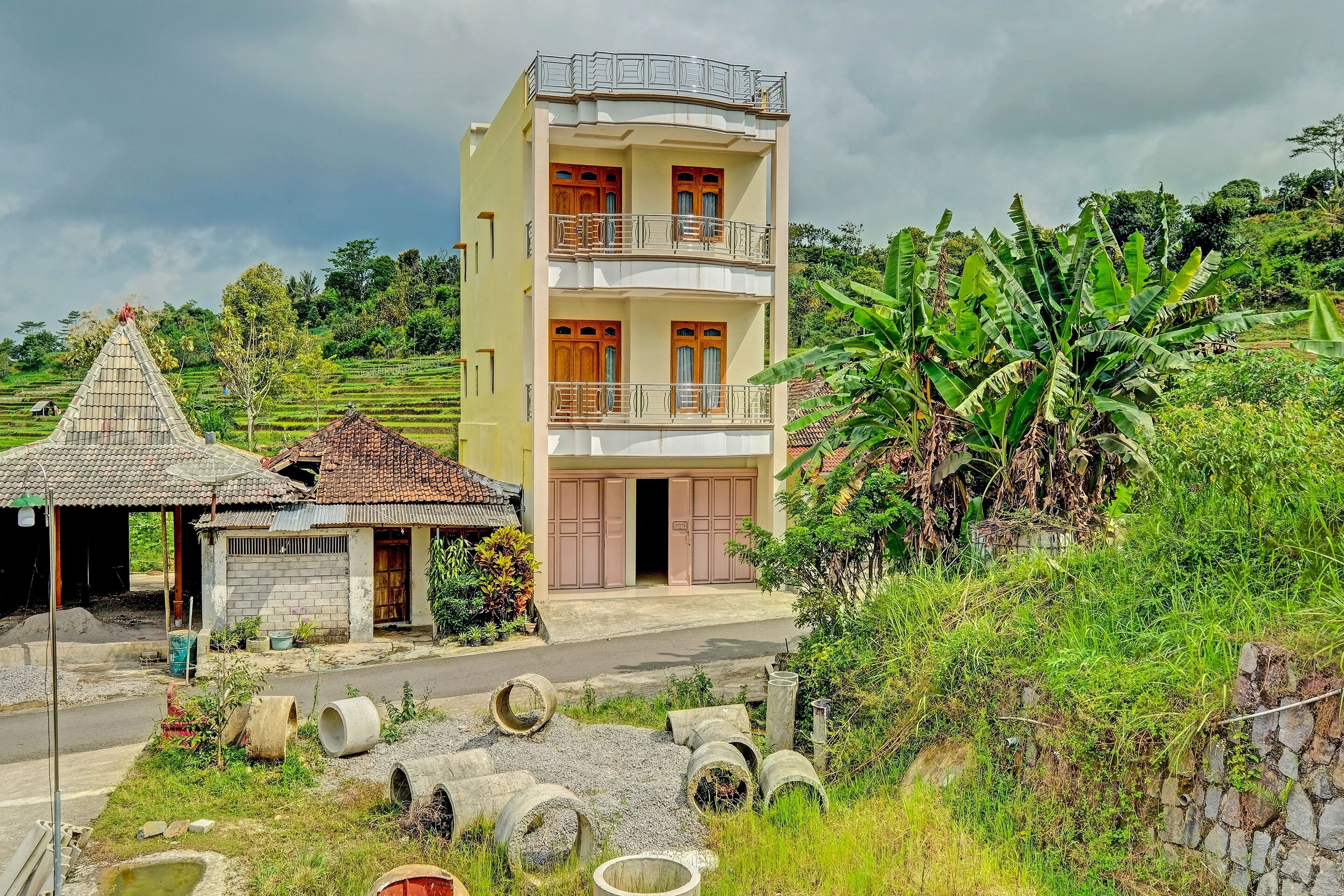 A multi-story building with balconies, a small adjacent structure, and a road in the foreground.
