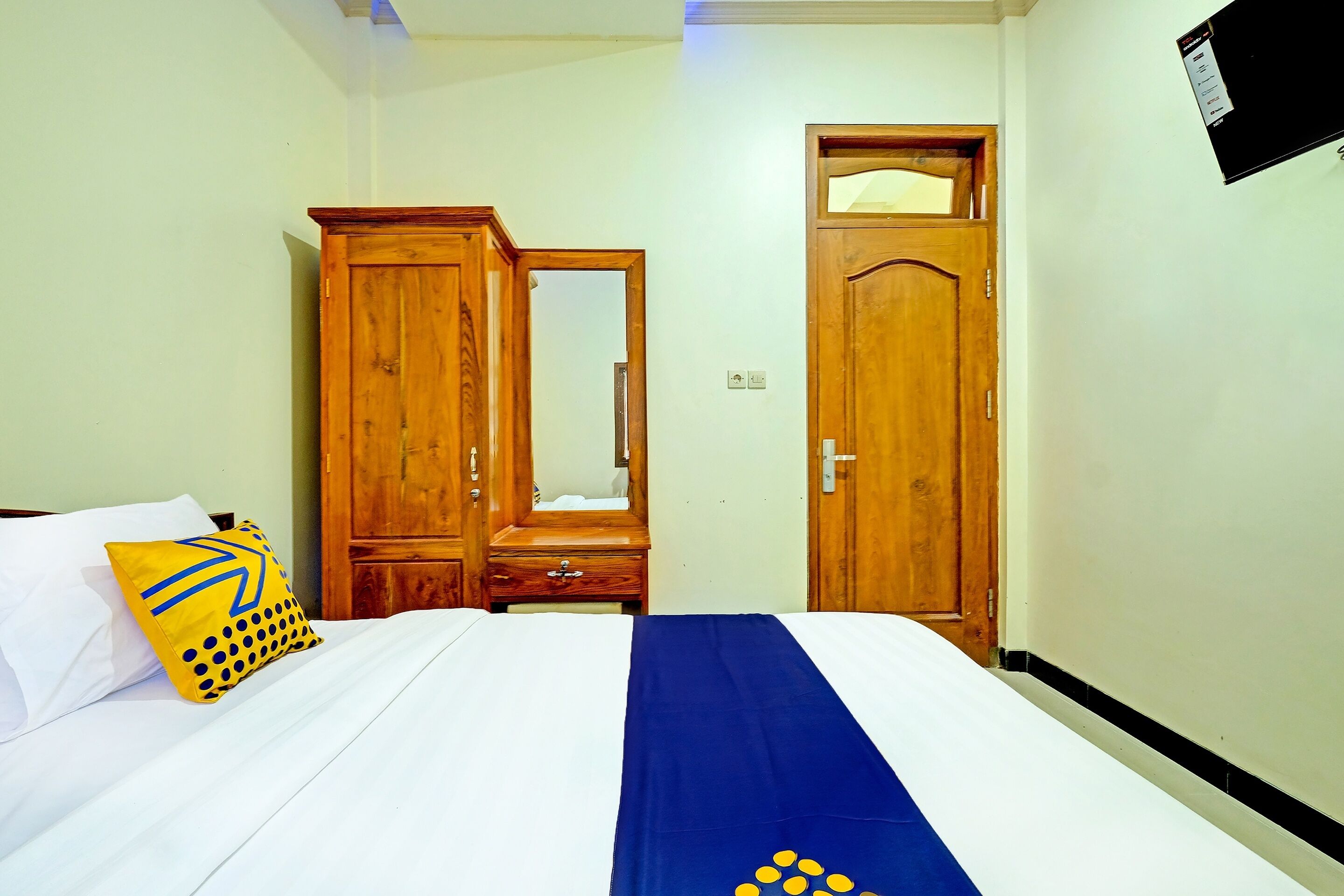 A bedroom with a bed, a wooden wardrobe, a mirror, and a door.