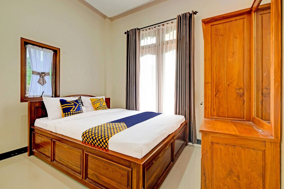 Ein ordentlich bezogenes Bett mit hölzernem Kopfteil, einem Holzschrank und einem gerahmten Bild an der Wand.