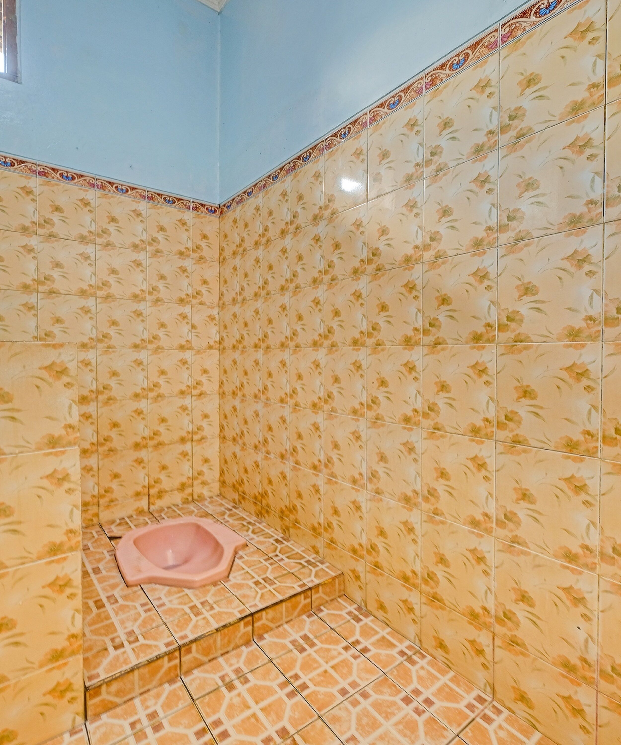 A bathroom with floral patterned tiles, a pink toilet, and a tiled floor.