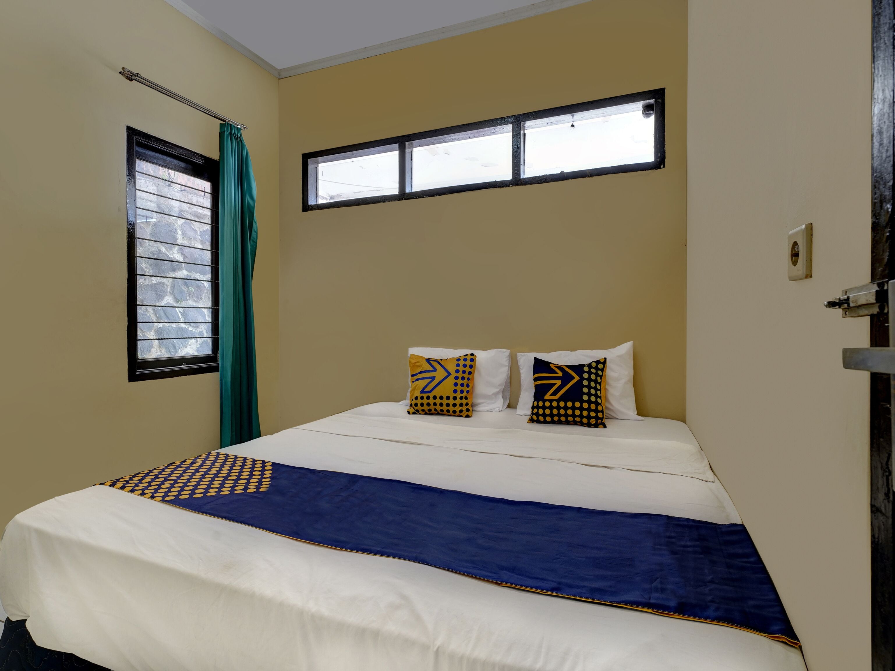 A hotel room with a bed, two pillows, a window, and a curtain.
