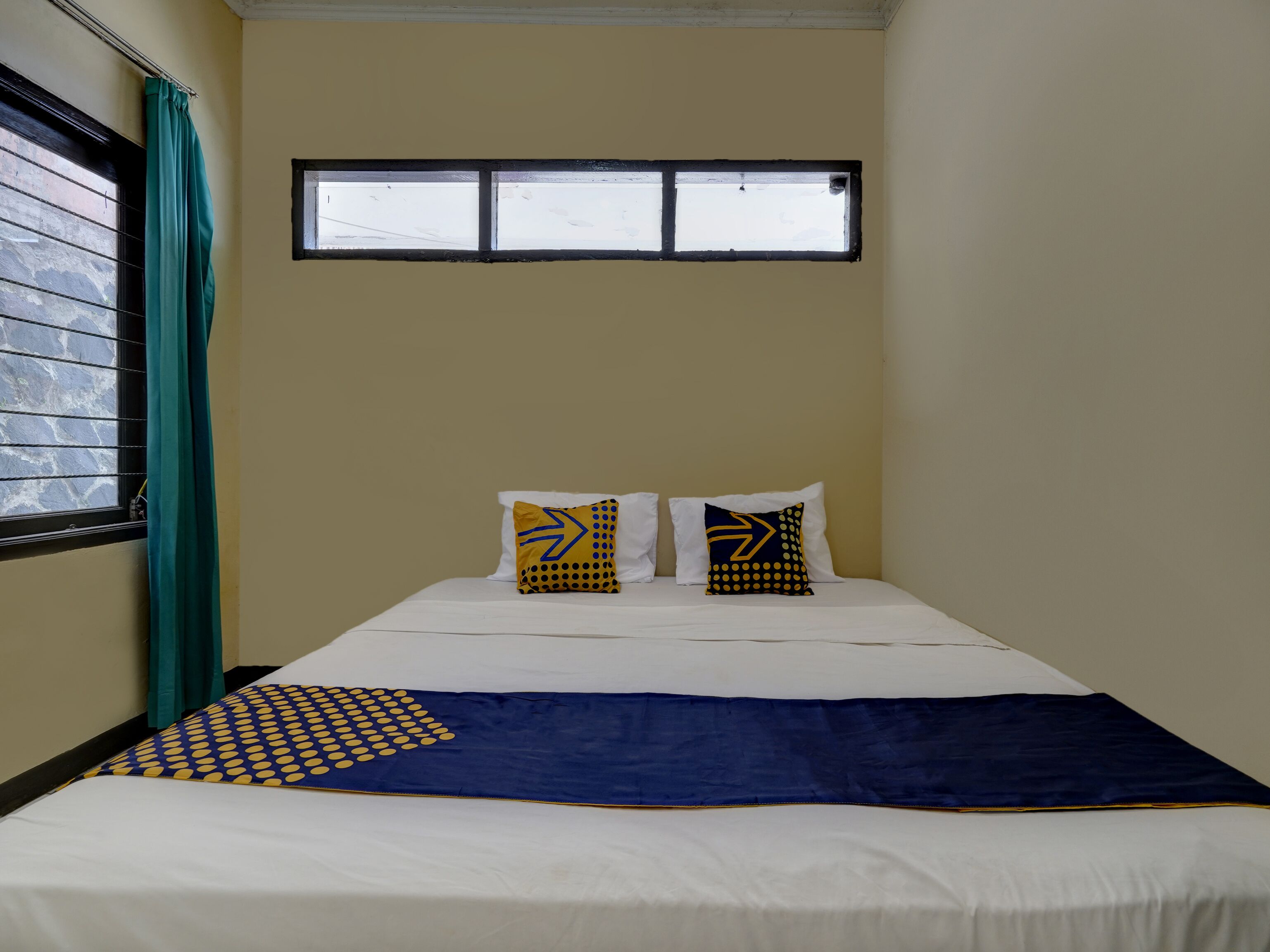Ein Zimmer mit einem Bett, zwei Kissen, einem Fenster und einem Vorhang.