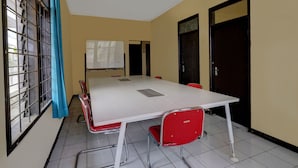 A conference room with a white table, red chairs, a whiteboard, and a window with metal bars. - OYO Life 91116 Pelangi Residence Syariah (Hegarmanah)