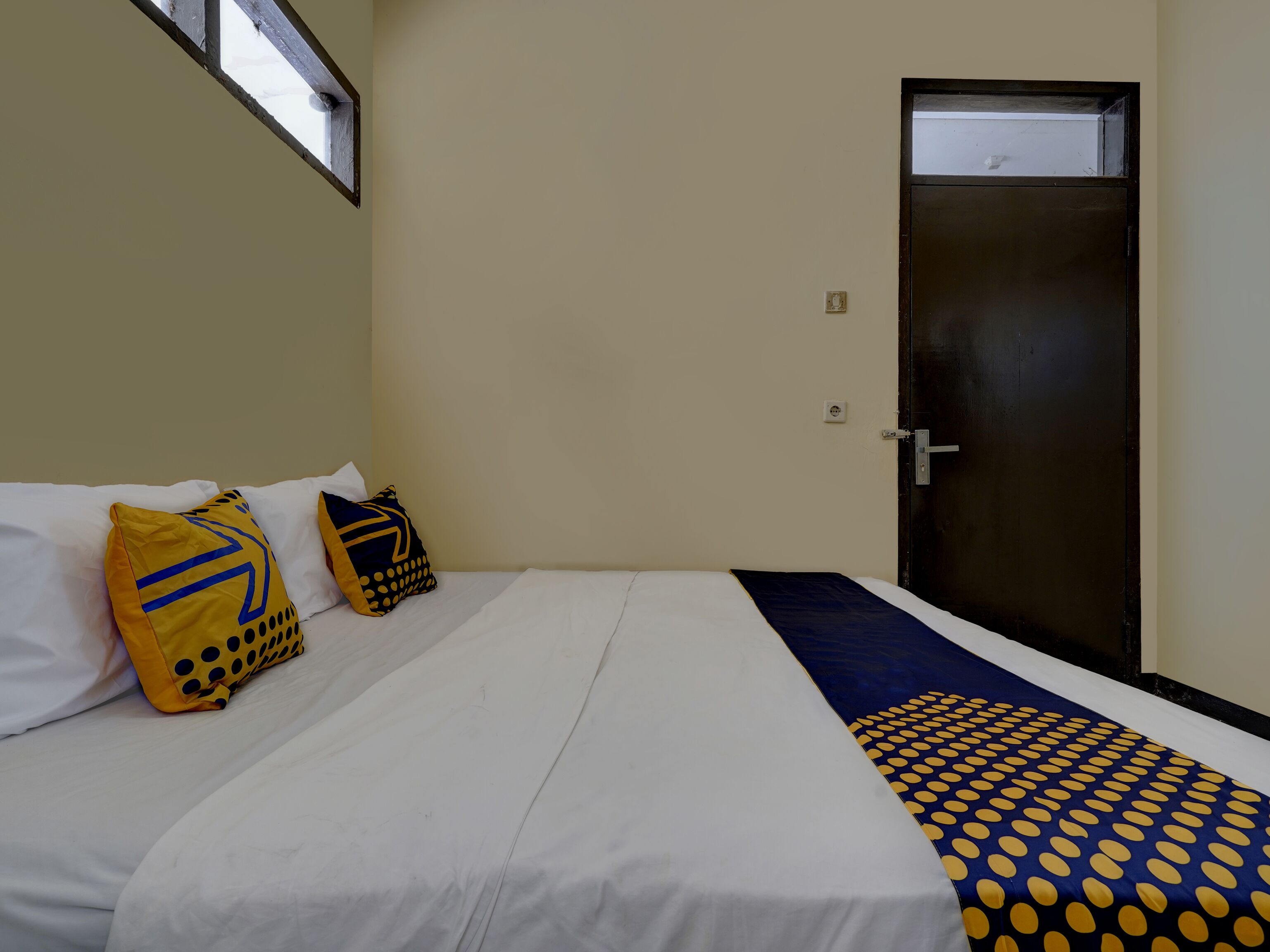 A hotel room with a bed, two pillows, a door, and a window.