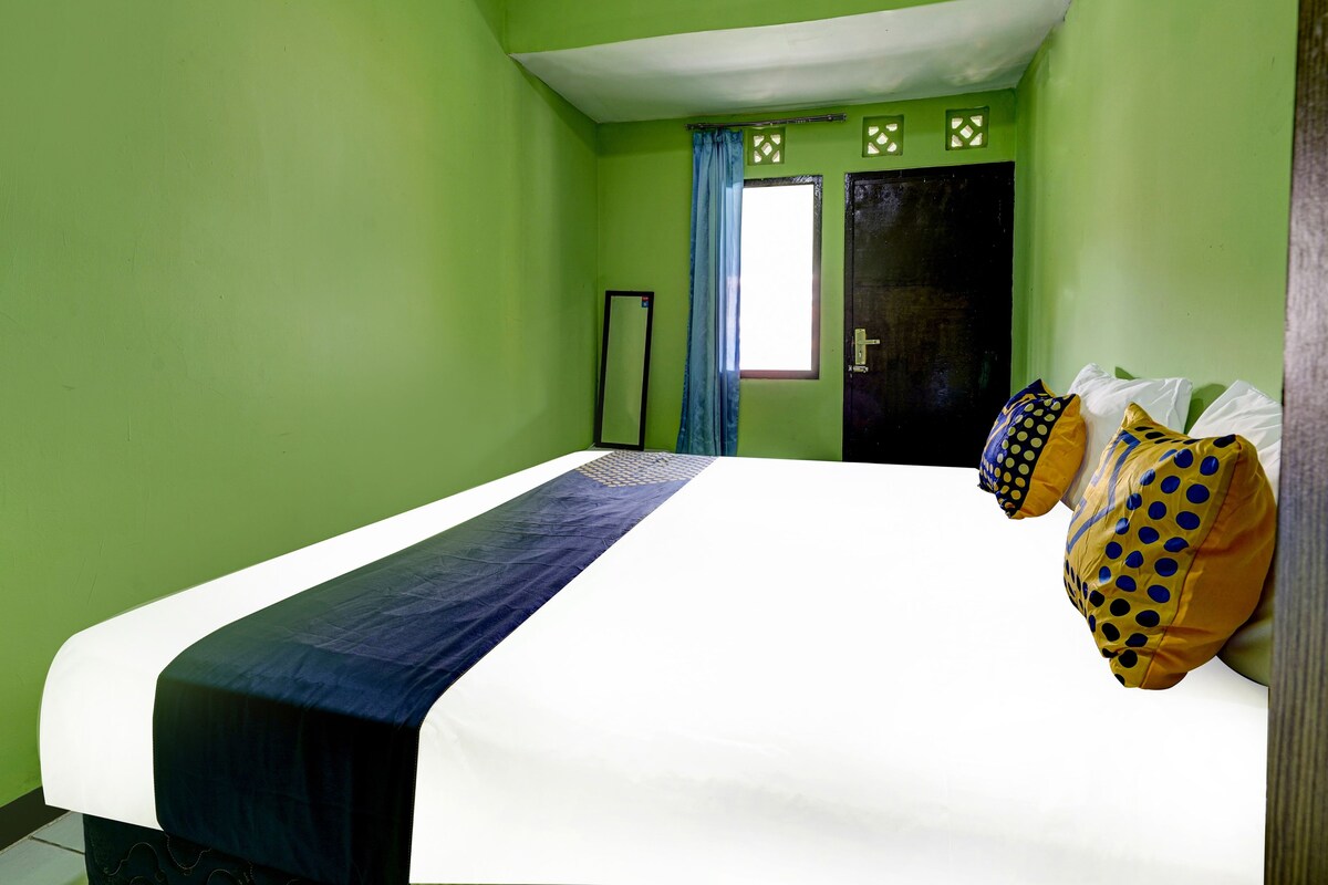 A room with green walls, a bed with a white and blue bedspread, and two pillows with polka dots.