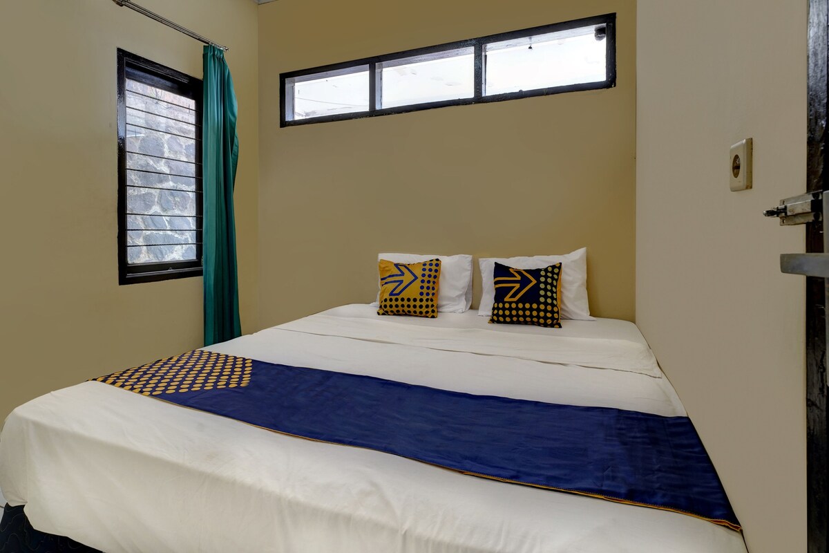 Una habitación de hotel con cama, ventana con cortinas y una lámpara de pared.