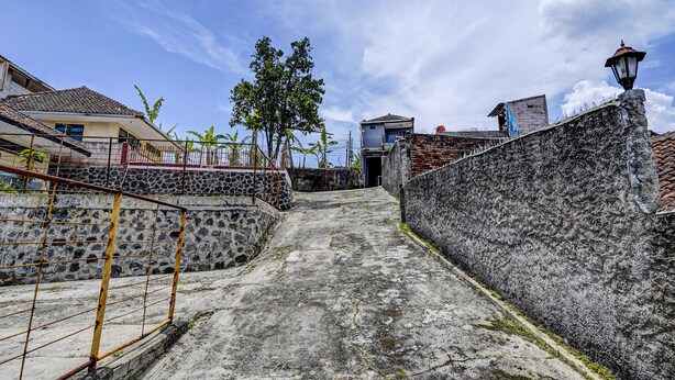 A narrow alleyway with stone walls, a metal fence, and a pathway leading to a building entrance. - OYO Life 91116 Pelangi Residence Syariah (Hegarmanah)