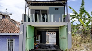A two-story building with a balcony, a green door, and a small shop at the entrance. - OYO Life 91116 Pelangi Residence Syariah (Hegarmanah)