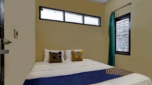 A neatly made bed with a blue and white bedspread, two pillows with geometric patterns, a window with a curtain, and a door with a handle. - OYO Life 91116 Pelangi Residence Syariah (Hegarmanah)