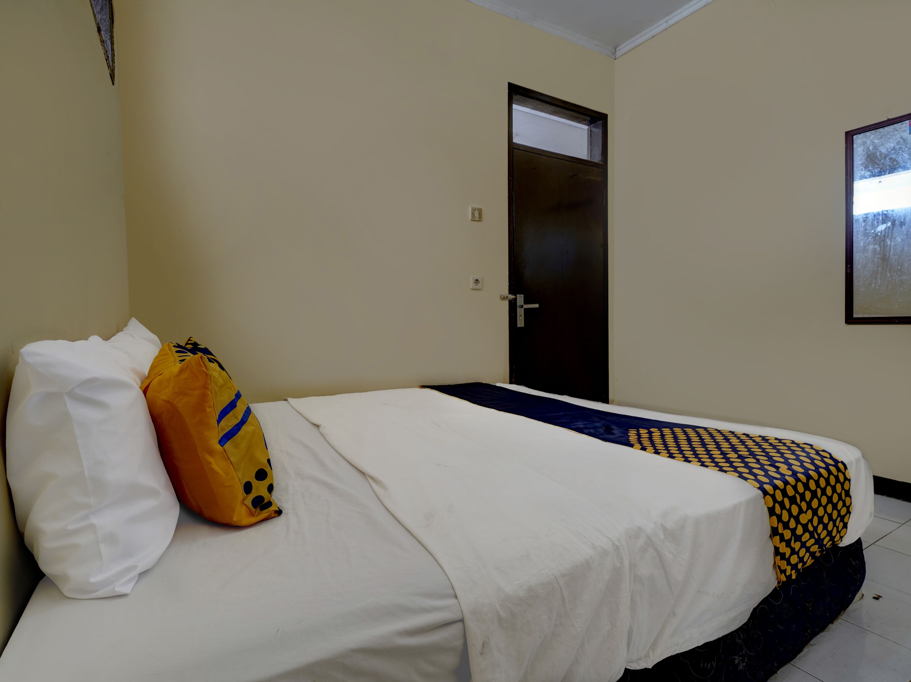 A hotel room with a bed, a pillow, a bag, and a door.