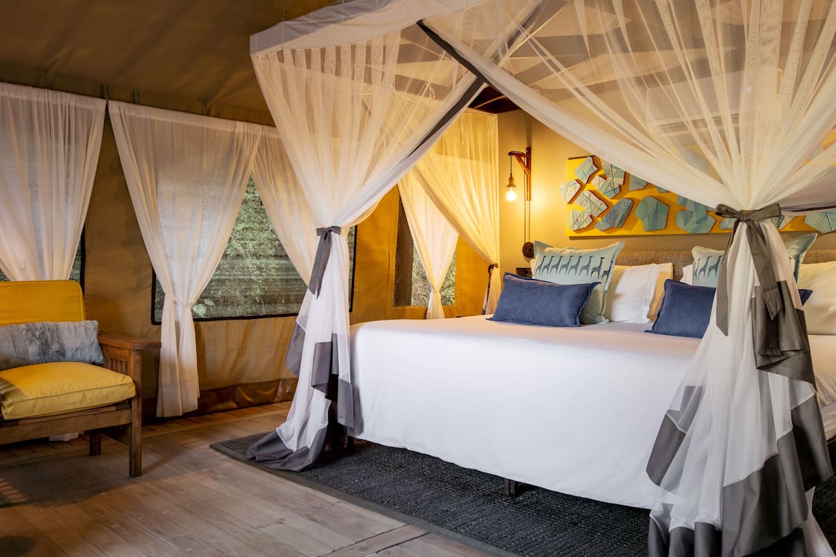 A bedroom with a canopy bed, a chair, and a wall with artwork.