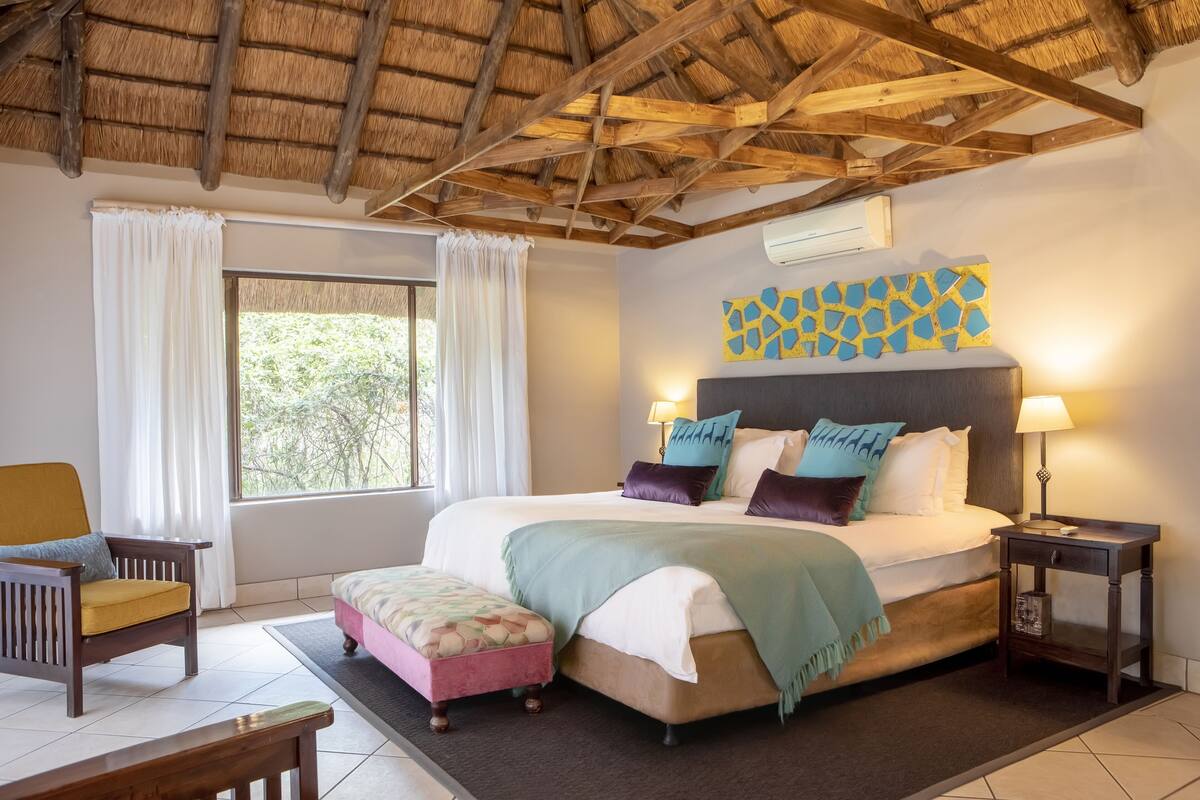 A bedroom with a bed, a chair, a nightstand, and a window.