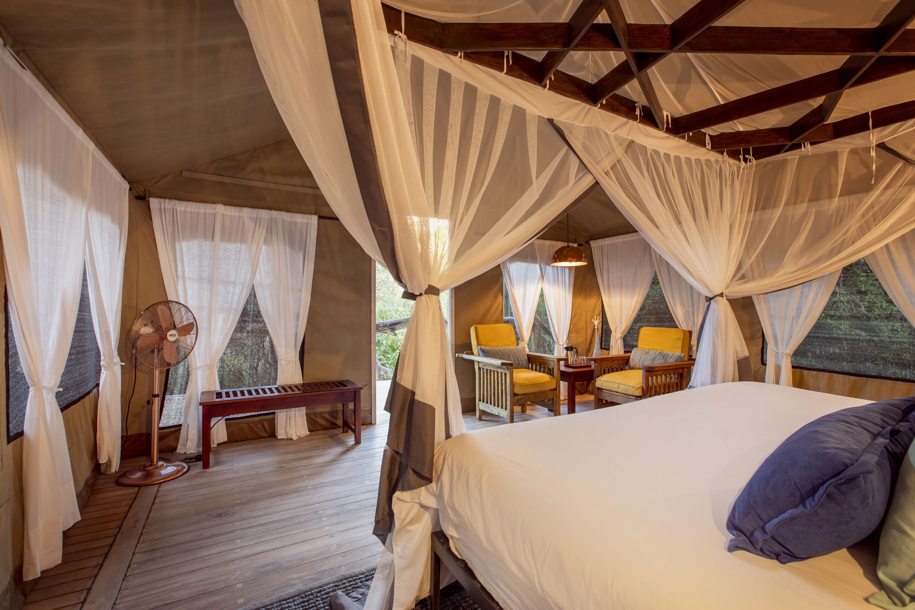 A bedroom with a bed, a fan, a bench, and a table with chairs.