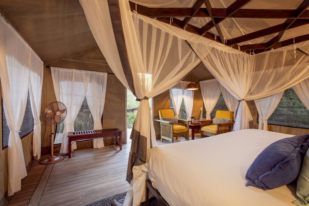 A bedroom with a bed, a fan, a bench, and a table with chairs.