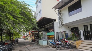 A street view with parked motorcycles, a food stall, and buildings with balconies. - SPOT ON 92092 Wisma Nilam Sari Syariah (Batam)
