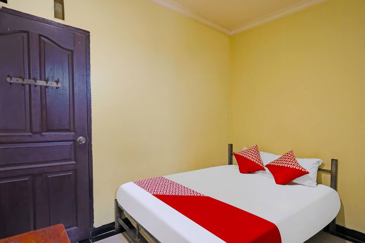 Una habitación con cama, puerta de madera y pared amarilla.