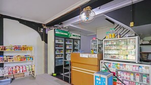 A store interior with shelves stocked with various products, a refrigerated display case, and a fan on the ceiling. - SPOT ON 92092 Wisma Nilam Sari Syariah (Batam)