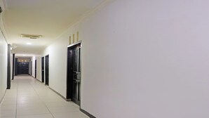 A long, narrow hallway with white walls and tiled floors, leading to a door at the end. - SPOT ON 92092 Wisma Nilam Sari Syariah (Batam)