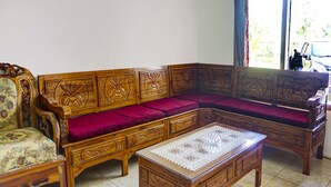 Een traditionele houten bank met ingewikkelde houtsnijwerken, een bijpassende fauteuil, en een bijzettafeltje met een kant kleed.