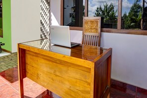 A wooden desk with a laptop, a chair with a carved design, and a window with a view of greenery. - Hotel O Desa Wisata KalipucangNearGreen Zone Indonesia (Purwosari)