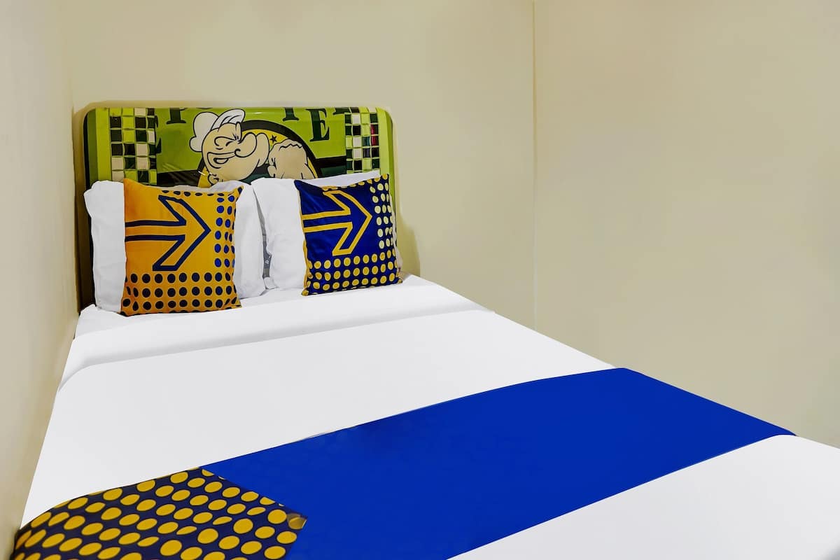 Una cama con una colcha blanca y azul, dos almohadas con diseños amarillos y azules, y un cabecero verde con un personaje de dibujos animados.