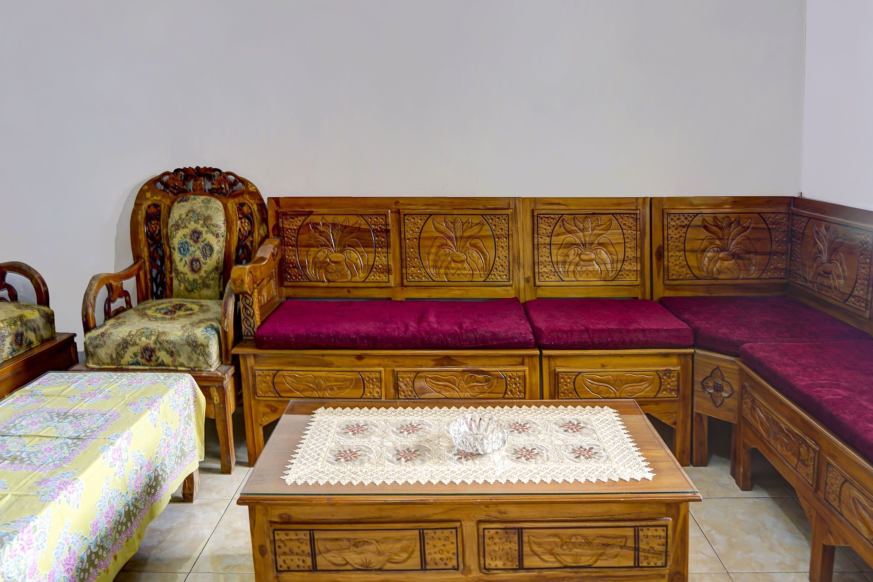Un canapé traditionnel en bois, orné de sculptures complexes, une table en bois assortie et une couvre-lit à motifs floraux.