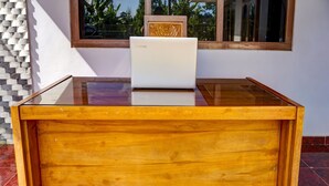 Een houten bureau met een laptop voor een raam met een decoratief hoofdeinde.