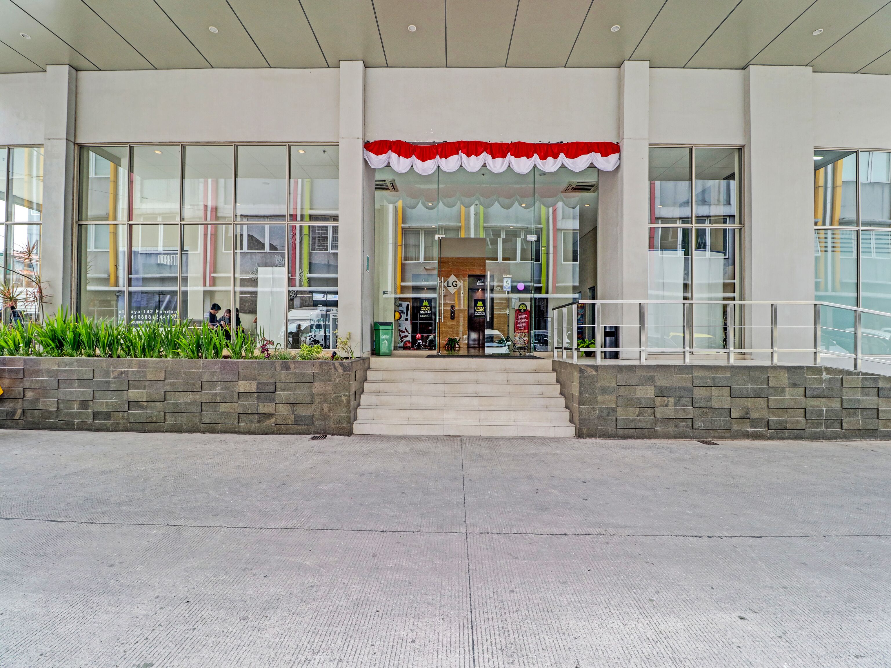 A modern building entrance with a red and white awning, large glass windows, and a staircase leading to the entrance.
