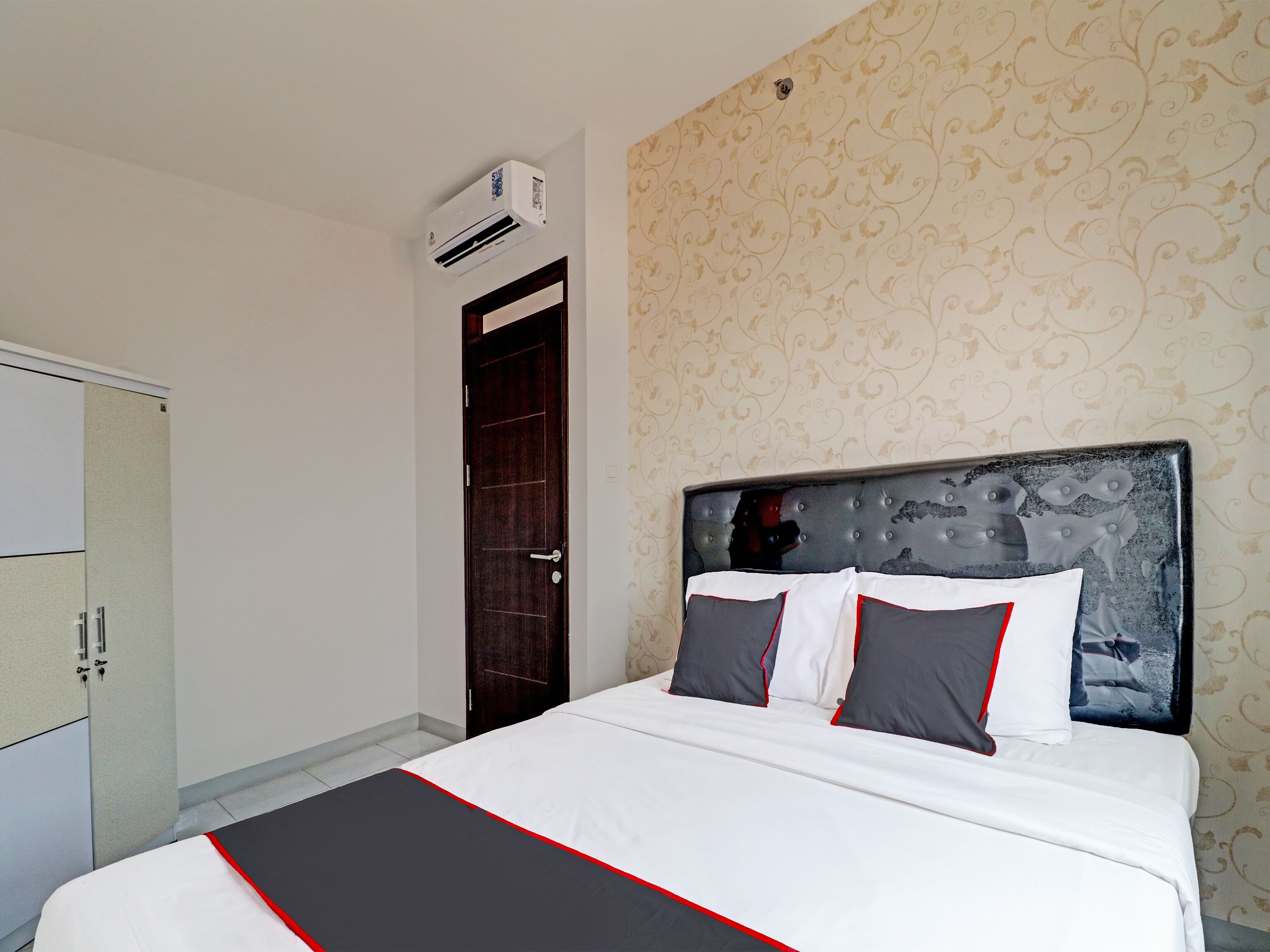 Un lit bien fait, recouvert d’une couvre-lit noire et blanche, avec une tête de lit en bois foncé et deux oreillers.