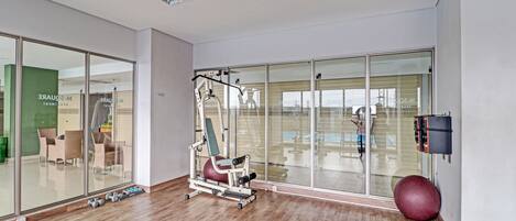 A modern fitness room with exercise equipment, a large mirror, and a glass wall.