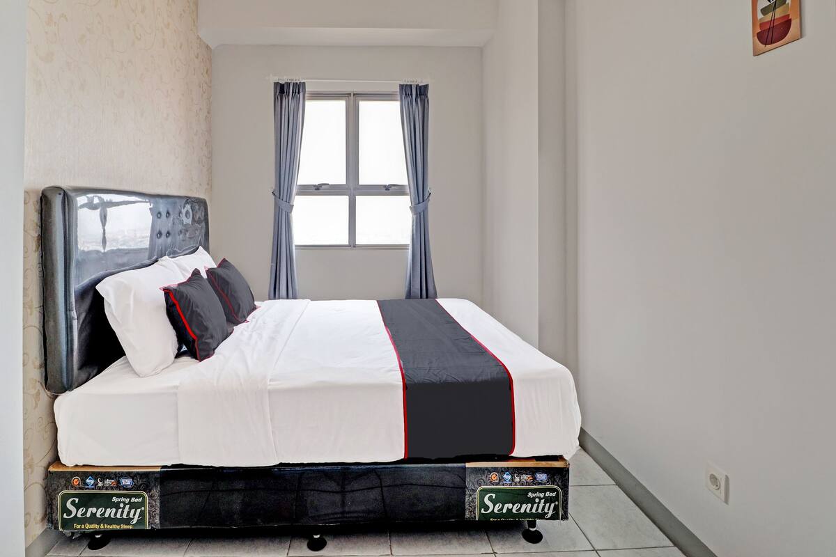 Una cama bien hecha con un colchón de marca, una ventana con cortinas y una pared lisa con un pequeño cuadro.