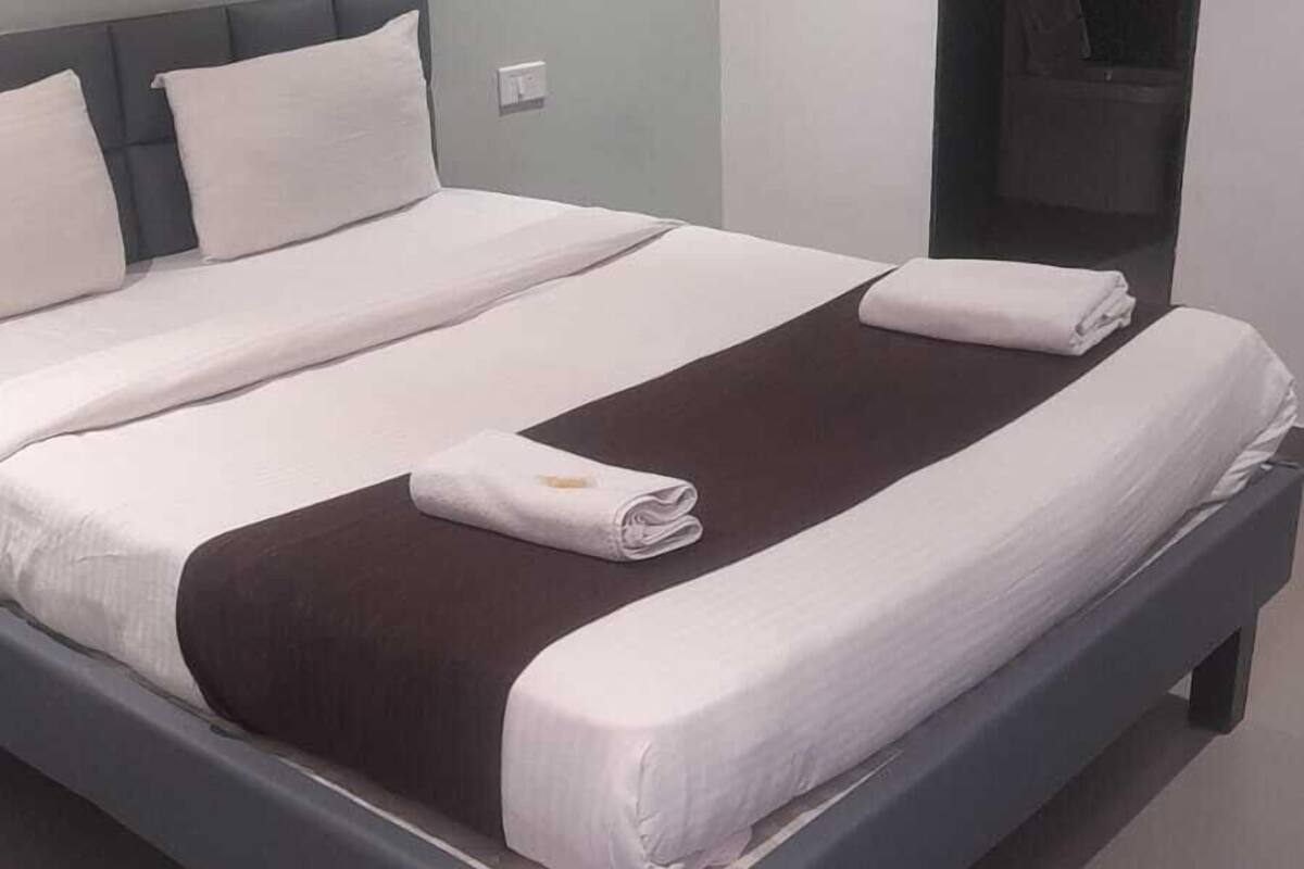 A modern hotel room with a large bed, a dark headboard, and a large mirror on the wall.