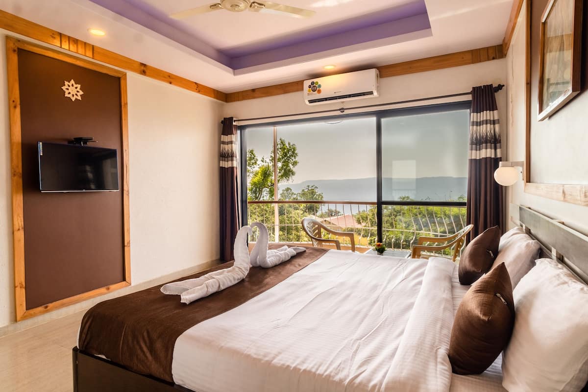 A hotel room with a large bed, a flat-screen TV, a balcony with a view, and an air conditioning unit.