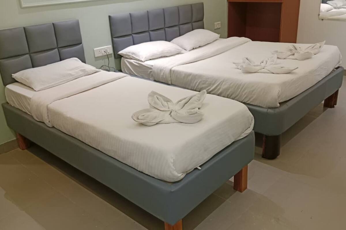 Two beds with grey headboards and white linens, a wooden nightstand, and a wall-mounted mirror.