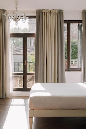 A bedroom with a large bed, a chandelier, and a view of a balcony with curtains. - iH Hotels Venezia Salute Palace (Venice)